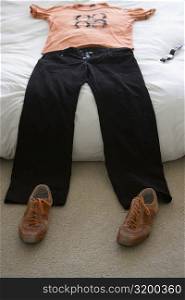T-shirt and jeans on the bed with a pair of shoes on the floor