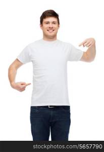 t-shirt design, gesture and people concept - smiling young man in blank white t-shirt pointing fingers on himself