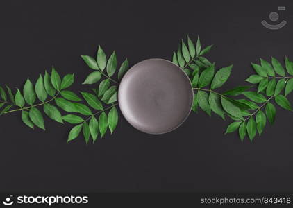 Table arrangement with an empty grey plate on tree twigs and black table. Food background. Empty tableware. Mockup. Above view of lunch settings.