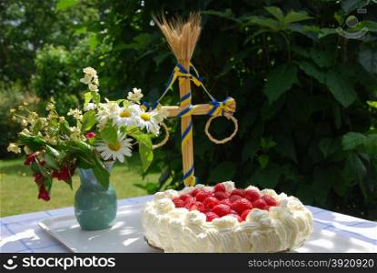 Table in a garden with a fresh strawberries cake, midsummer pole and flowers