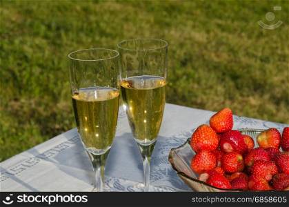 Table in a garden with two glasses sparkling wine and a bowl with fresh strawberries