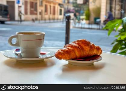Table of street cafe in Paris in the morning. Cup of coffee and croissant close-up. Background in defocus. Cup of Coffee and a Croissant on the Street Table