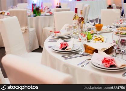 Table set for a wedding reception in white and red colors with gift on a plate. Wedding table decoration