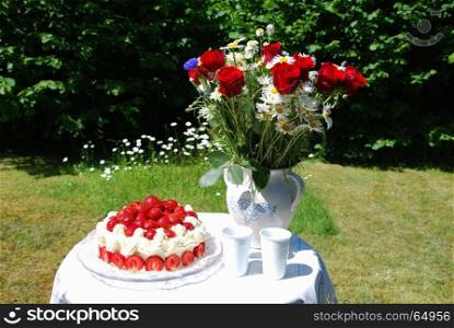 Table set for summer celebration outdoors with strawberry cake and a bouquet of summer flowers