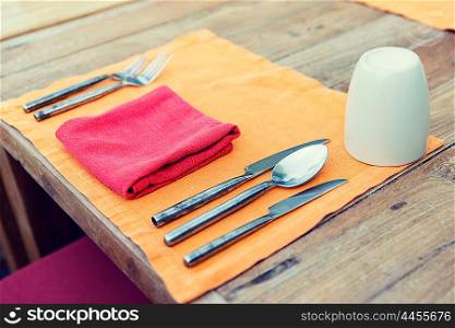 table setting, silverware and eating concept - close up of cutlery with glass and napkin on restaurant table