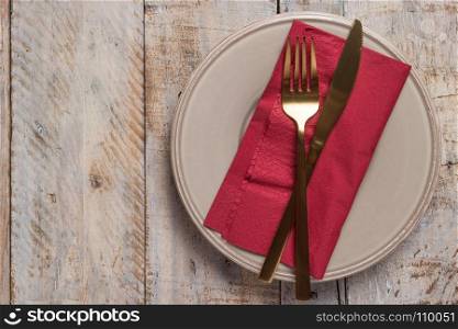 Table setting with plate golden fork and knife on wooden background
