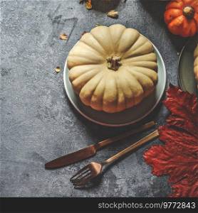 Table setting with pumpkin on plate with cutlery  and autumn leaves on dark rustic background, top view