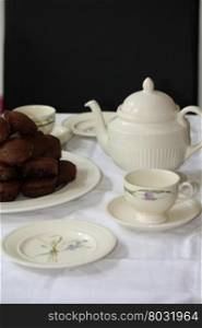 table setting with tea pot, tea cups and chocolate muffins