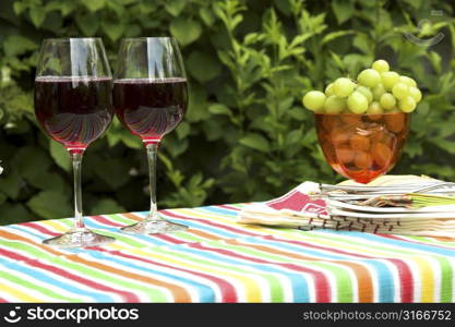 Table setup outdoors with two glasses of wine, a bowl of grapes and plates