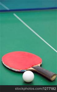 Table tennis racket with a ball on green background.