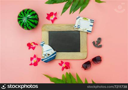 Table top view accessory plan to travel beach in summer holiday background concept.Flat lay palm leaf with many essential items flower & palm leaf on pink paper.Blackboard for creative design text.
