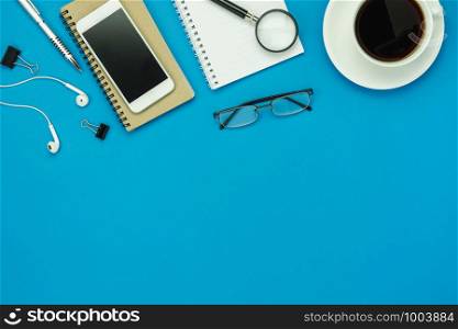 Table top view aerial image of accessories office desk background concept.Flat lay of variety object the mobile phone & pen and coffee with earphone on modern rustic blue paper with copy space.