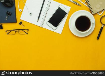 Table top view aerial image of accessories office desk background concept.Flat lay of variety object the mobile phone & pen and coffee with earphone on modern rustic yellow paper with copy space.