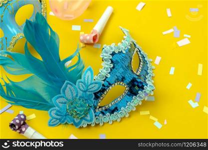 Table top view aerial image of beautiful colorful carnival season or photo booth prop Mardi Gras background.Flat lay object blue mask with decorations on yellow wallpaper.Free space for text mock up