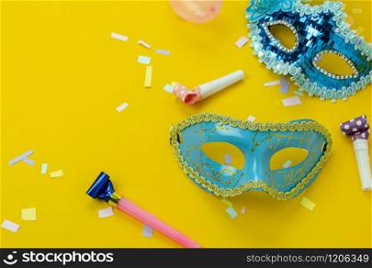 Table top view aerial image of beautiful colorful carnival season or photo booth prop Mardi Gras background.Flat lay object blue mask with decorations on yellow wallpaper.Free space for text mock up