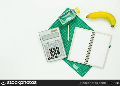 Table top view aerial image of count cal weight for sport fitness background concept.Flat lay essential objects paper clip & calculator with fresh water and banana on modern rustic white wooden.