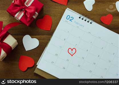 Table top view aerial image of decoration valentine&rsquo;s day background concept.Flat lay arrangement of calendar page of february month with essential items love heart with gift box on wooden.