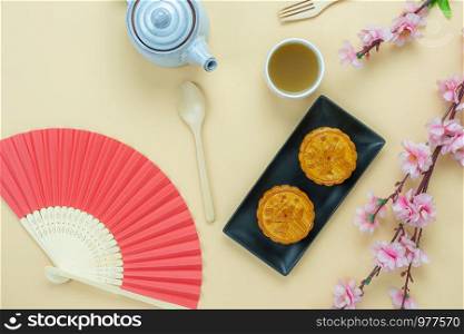 Table top view aerial image of decorations Chinese Moon Festival or lunar new year background concept.Flat lay essential meal set of green tea with sweet moon cake & flower on yellow paper and space.