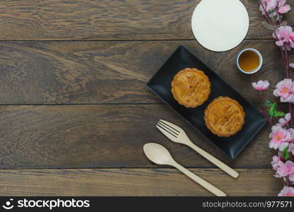 Table top view aerial image of decorations Chinese Moon Festival or lunar new year background concept.Flat lay essential meal set for coffee break of sweet cake & tea with blossom on brown wooden.