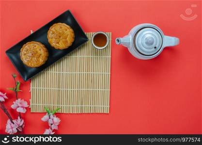 Table top view aerial image of decorations Chinese Moon Festival or lunar new year background concept.Flat lay essential meal set for coffee break of sweet cake & tea with pink blossom on red paper.