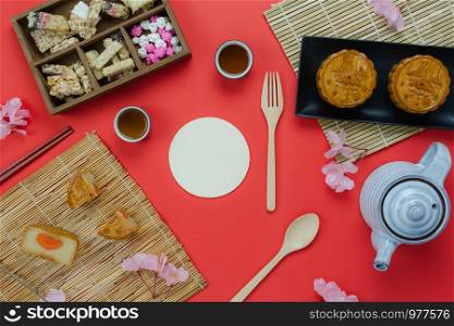 Table top view aerial image of decorations Chinese Moon Festival or lunar new year background concept.Flat lay essential meal set for coffee break of sweet cake & tea with blossom on red paper.