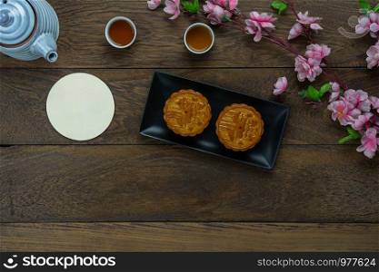 Table top view aerial image of decorations Chinese Moon Festival or lunar new year background concept.Flat lay essential meal set for coffee break of sweet cake & tea with blossom on brown wooden.