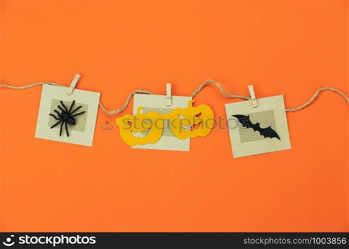 Table top view aerial image of decorations Happy Halloween day background holiday concept.Flat lay objects to party pumpkins photo prop and spider & bat hang on paper clips on orange wallpaper.