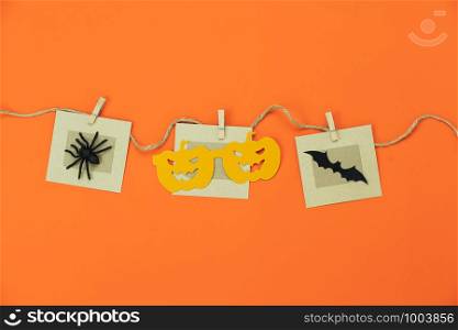 Table top view aerial image of decorations Happy Halloween day background holiday concept.Flat lay objects to party pumpkins photo prop and spider & bat hang on paper clips on orange wallpaper.