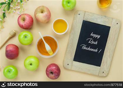 Table top view aerial image of decorations Jewish holiday the Rosh Hashana background concept.Flat lay apple & honey bee cup and wood spoon on modern yellow paper.Text design season on blackboard.