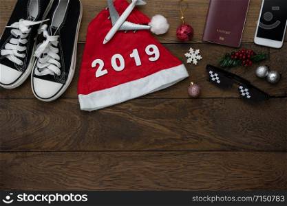 Table top view of Merry Christmas decorations & Happy new year 2019 ornaments concept.Flat lay essential difference objects to travel text & gift box with clothing on modern wooden brown background.
