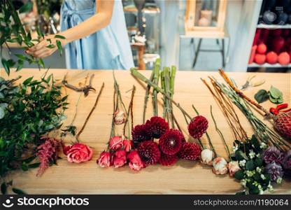 Table with fresh flowers of different varieties in floral shop, female florist on background. Flowers arrangement making