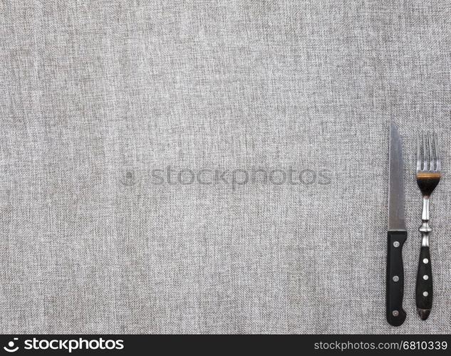 Tablecloth from rough linen fabric with a fork and knife. Creative background for banner or menu cafe or restaurant.. Tablecloth from rough linen fabric with a fork and knife. Creative background for banner or menu cafe or restaurant