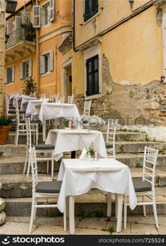 Tables and chairs of small neighborhood cafe in Kerkyra. Small empty taverna in Old Town Corfu