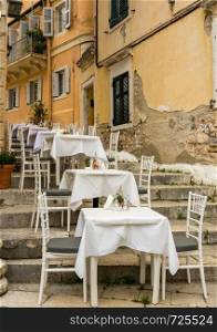 Tables and chairs of small neighborhood cafe in Kerkyra. Small empty taverna in Old Town Corfu