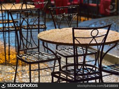 Tables at an outdoor cafe in the rain, illuminated bright backlighting. Prague.