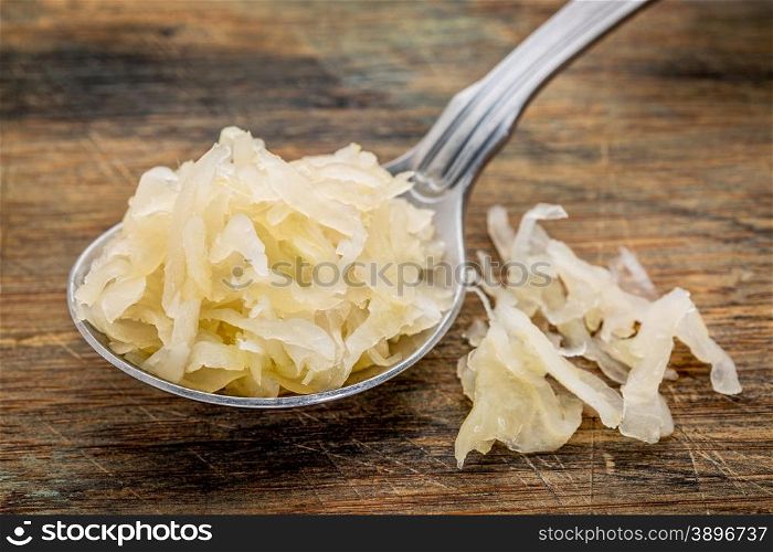 tablespoon of sauerkraut against rustic wooden cutting board - healthy eating concept