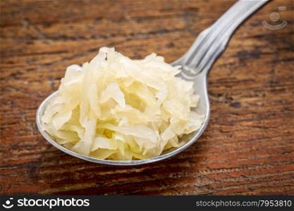 tablespoon of sauerkraut against rustic wooden cutting board - healthy eating concept (probiotic food)