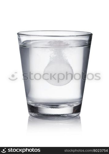 Tablet dropped into the water. Glass with effervescent tablet in water with bubbles on white background