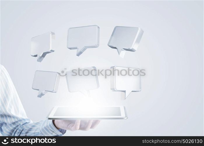 Tablet in hand with symbols. Close up of businessman hand holding tablet and glass speech symbols