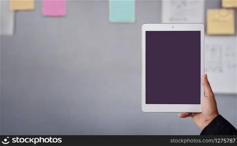 Tablet Mockup Image. Display Screen is Clipping Path. Modern Businesman Using Tablet in Office. Blurred Sticky Note and Project Planning on the Wall as background