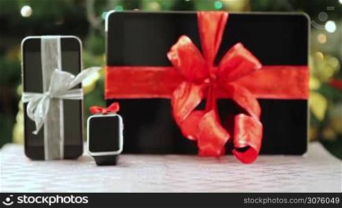 Tablet pc, smartphone and smartwatch as gifts in front of Christmas tree with lights.