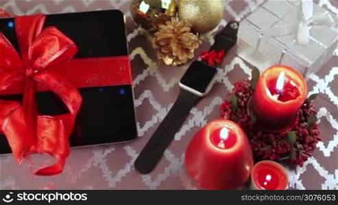 Tablet pc, smartphone and smartwatch for Christmas with gifts, decorations and candles on table.