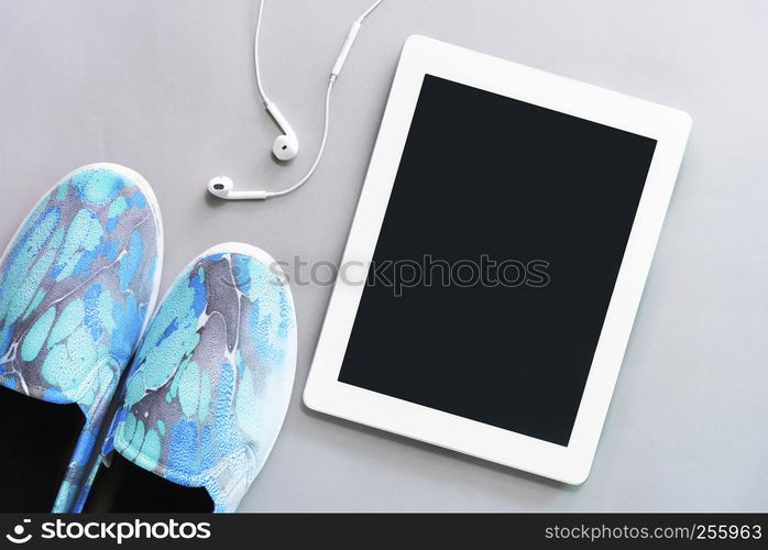 Tablet with earphone with blue sneaker on floor. Technology, listening to music and lifestyle concept.