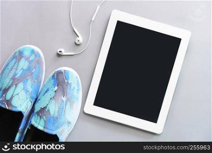 Tablet with earphone with blue sneaker on floor. Technology, listening to music and lifestyle concept.