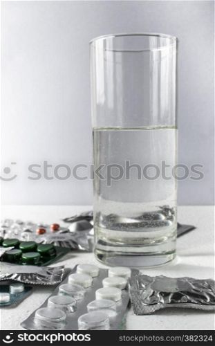 Tablets in packs on a white background near a glass of water. Pills. Closed pills in pack.. Tablets in packs on a white background near a glass of water. Pills.