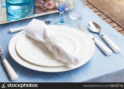 Tableware - set of white plates, cups and utencils on blue tablecloth