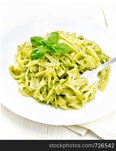 Tagliatelle pasta with pesto, basil and fork in a plate on a napkin on wooden board background