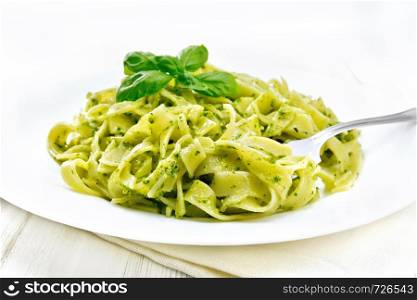 Tagliatelle pasta with pesto, basil and fork in a plate on a towel on the background of wooden boards