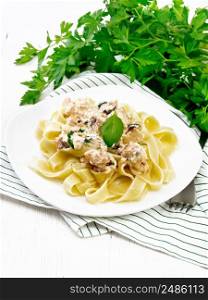 Tagliatelle pasta with salmon, cream, garlic and herbs in a plate on a kitchen towel, fork, parsley and basil on wooden board background