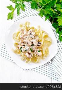 Tagliatelle pasta with salmon, cream, garlic and herbs in a plate on a towel, fork, parsley and basil on a white wooden board background from above